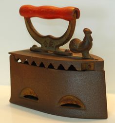 an old fashioned iron with a red handle and a small bird on it's side