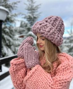 a woman wearing a pink sweater and hat while holding her hands up to her ear