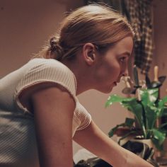 a woman sitting in front of a laptop computer on top of a wooden table next to a potted plant