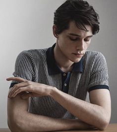 a young man sitting at a table with his hand on his elbow and looking down