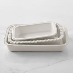 three white dishes with scalloped edges on a marble countertop, one is empty