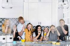 a group of people sitting on top of a kitchen counter with food in front of them