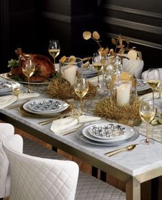 a table set with white and gold plates, silver napkins, wine glasses and candles