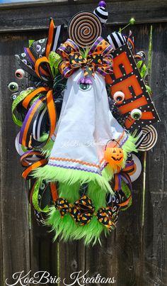 a halloween wreath hanging on the side of a wooden fence with an orange and green decoration