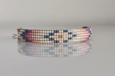 a pink, blue and white beaded bracelet with gold clasps on a reflective surface