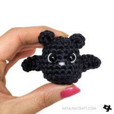 a hand holding a small black crocheted teddy bear with big eyes and ears