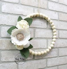 a white flower and beaded necklace hanging on a brick wall next to a wooden bead wreath