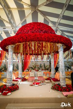 a wedding setup with red flowers on the table and white draping over it