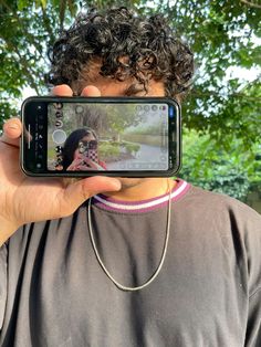 a man taking a selfie with his cell phone in front of him, under a tree