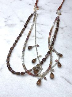 A beautiful three stranded necklace: . the longer strand consists of silver fill rollo chain with lovely faceted smoky quartz teardrop dangles. The other two strands consist of smooth Botswana agate rounds and faceted smoky quartz rectangles. More agate rounds dangle from both edges. The necklace is completed with tan leather cords. The necklace measures 26" and the length is variable using sliding knots. Multi-strand Crystal Necklaces With Faceted Beads, Multi-strand Crystal Necklace With Faceted Beads, Bohemian Silver Briolette Necklaces, Silver Multi-strand Beaded Necklaces With Natural Stones, Bohemian Multi-strand Silver Crystal Necklaces, Bohemian Multi-strand Silver Crystal Necklace, Bohemian Silver Multi-strand Crystal Necklaces, Silver Drop Necklaces With Faceted Beads, Silver Multi-strand Necklace With Natural Stones