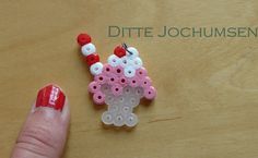 a hand holding a pink and white beaded brooch on a wooden table with the words ditte jochumsen written above it