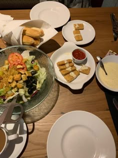 a wooden table topped with lots of plates and bowls filled with different types of food