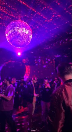 people are dancing in a disco ball with purple lights and confetti on the ceiling