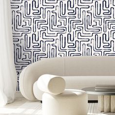 a white couch sitting next to a table in front of a wall covered in black and white designs