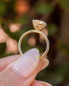 a woman's hand holding a gold ring with a flower design on the side