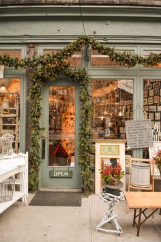 an open store front with lots of plants and decorations on the outside windows, along with chairs and tables