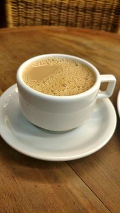 two cups of coffee sitting on top of a wooden table next to eachother