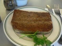 a white plate topped with meat next to a fork and knife on top of a table