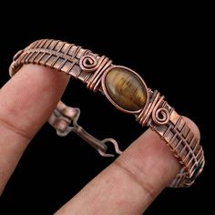 a close up of a person's hand holding a bracelet with a tiger eye stone