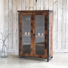 a wooden cabinet with glass doors in front of a wood paneled wall and vase