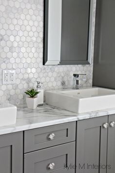 a bathroom with gray cabinets and white hexagonal tiles on the wall, along with a square sink