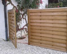 two wooden gates in front of a white building with flowers growing on the side of it