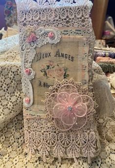 a card holder made out of lace and fabric with pink flowers on the front, sitting on top of a doily covered table