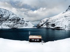 a small house sitting on top of a snow covered hill next to a body of water