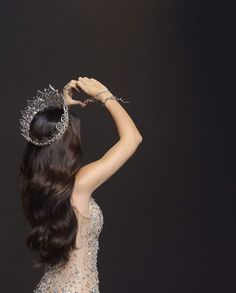 a woman wearing a tiara and holding her hair in the air