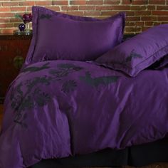 a bed with purple sheets and pillows in front of a brick wall