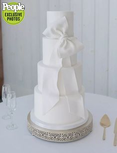 a white wedding cake sitting on top of a table next to wine glasses and utensils