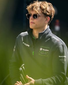 a young man wearing sunglasses and holding something in his hand while looking off into the distance