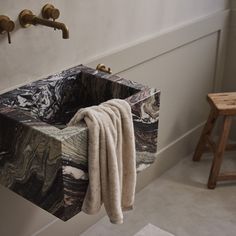 a marble sink in a bathroom next to a wooden stool and wall mounted faucet