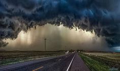 a very large storm moving across the sky over an empty road with cars on it