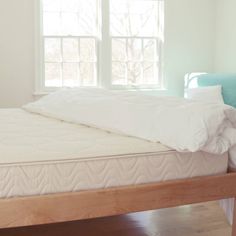 a bed with white sheets and pillows in a room next to a blue chair on the floor