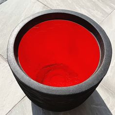 a black bowl with red liquid in it sitting on the ground next to a white tile floor