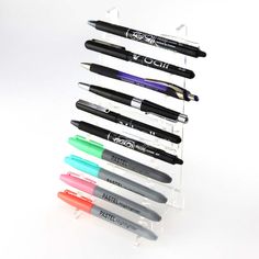 several pens are lined up in a clear holder on a white surface, with one pen sticking out of the top