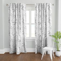 a white chair sitting in front of a window covered in birch tree print curtain panels