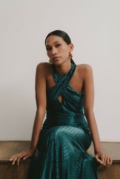 a woman sitting on top of a wooden table wearing a green dress and gold earrings