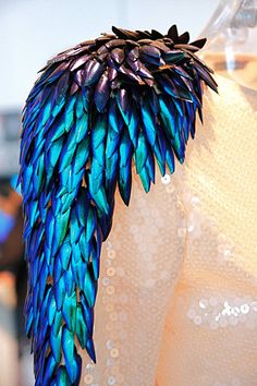 a dress with blue and green feathers on it's back, sitting on a mannequin