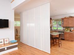 an open concept living room and kitchen with wood floors, white sliding doors, hardwood flooring and large flat screen tv mounted on the wall