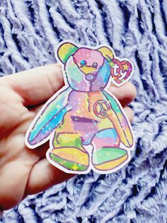 a hand holding a sticker with a colorful teddy bear on it's side