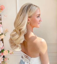 a woman with long blonde hair standing in front of a flowered wall and looking off to the side