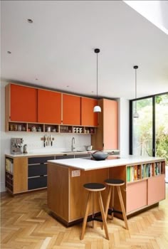 an orange kitchen with two stools in front of the island and cabinets on both sides