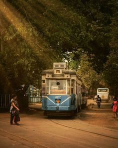 people walking on the side of a road near a blue trolley car and trees in the background