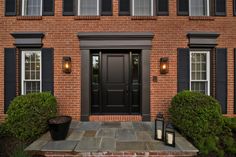 a brick house with black shutters and two lanterns on the front porch, next to a planter full of flowers