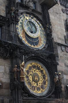 a large clock on the side of a building with statues around it's sides