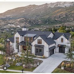 a large white house with black roof and two car garages in front of mountains