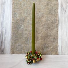 a green candle is sitting on a table next to some christmas balls and berries in front of a burlap background