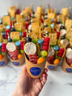 a hand holding up an ice cream cone filled with fruit and crackers in it